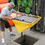 A construction professional fitting the EconoSack straps around a storm grate and guiding it back into the catch basin