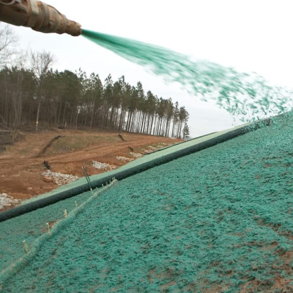 Mulch with tackifiers being sprayed out of a high-pressure hose to cover a large space of exposed soil