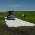 A construction truck driving on mud mats in a green field