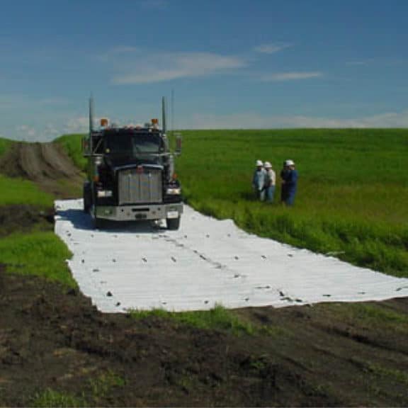 A construction truck driving on mud mats in a green field