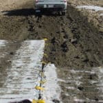 Construction trucks traveling across a muddy and rutted area without getting stuck due to the mud mats that are laid down