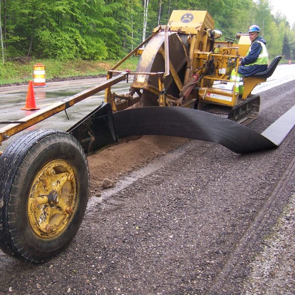 Construction workers installing strip drains to remove water from the surface of a road