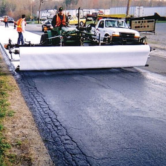 Construction crew using paving fabrics to retard reflective cracking & extend the life of the new asphalt